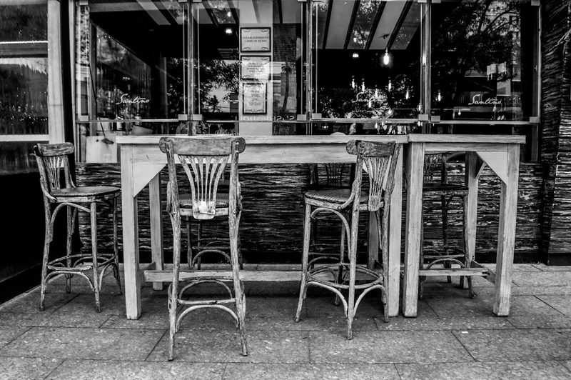 Black and white image of a rustic outdoor bar with wooden stools and high table in Mexico City