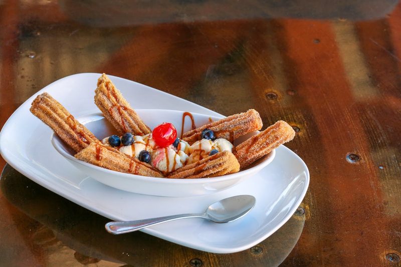 Plate of churros served with ice cream blueberries and a cherry