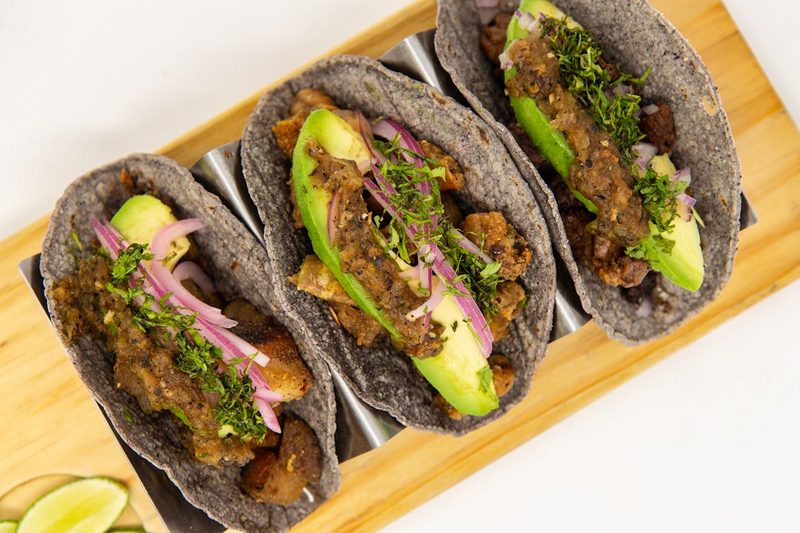 Close-up of blue corn tacos with avocado and fresh vegetables on a metal tray