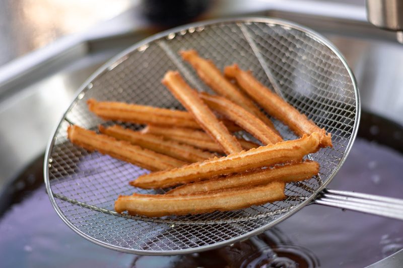 Freshly fried churros being drained on a wire skimmer ready to serve