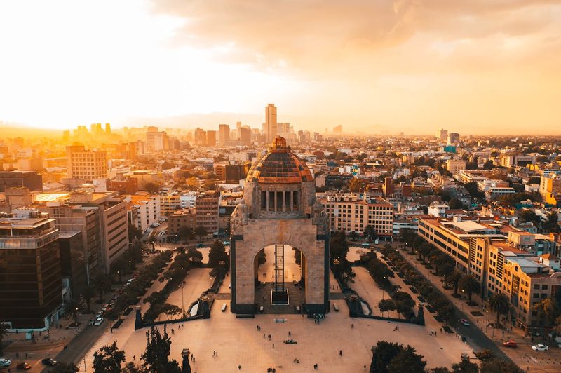 Monument to the Revolution silhouetted against a warm sunset with people in the plaza